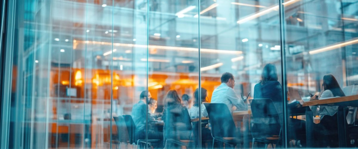 A group of people seated at a table in front of a transparent glass wall, potentially for work or meeting purposes